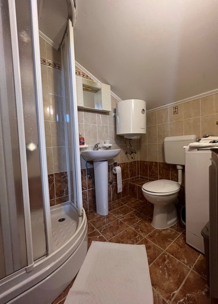 Fürdőszoba zuhanyzóval és barna csempével.