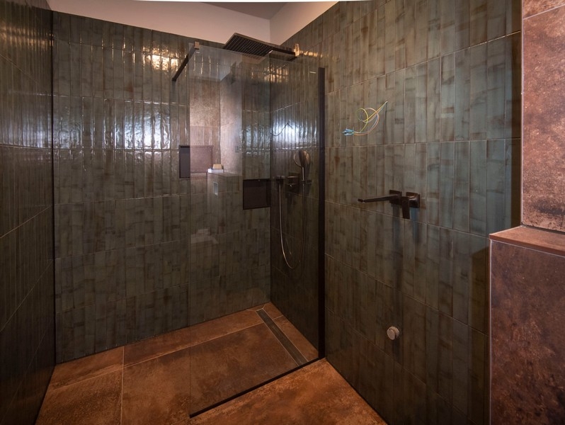 Fürdőszoba tágas zuhanykabinnal egy modern lakásban eladó a horvátországi Splitben, sötét csempével.