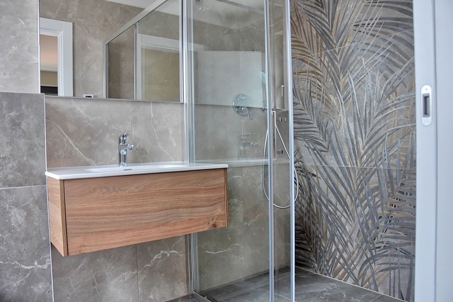 Modern fürdőszoba egy isztriai penthouse-ban dekoratív üvegcsempével díszített zuhanykabinnal és fa mosdóval.