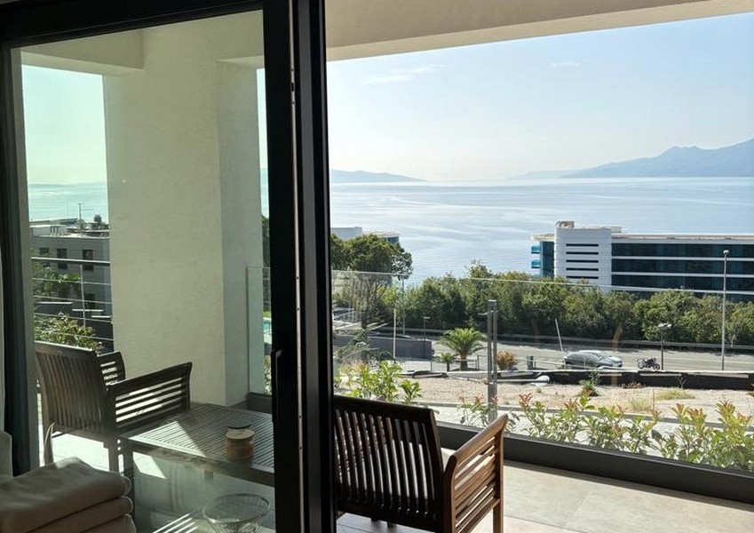 Erkély fa székekkel és tengerre néző kilátással egy nyitott üvegajtón keresztül, ingatlanhirdetés Rijekában, Horvátországban.