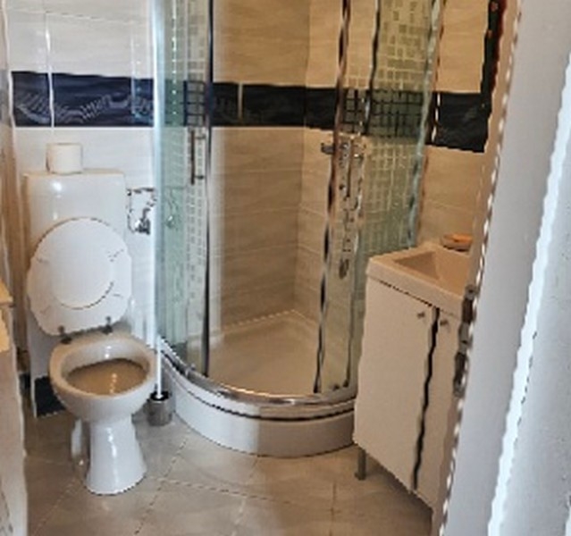 Fürdőszoba íves zuhanykabinnal, wc és mosdó a járólapos szobában