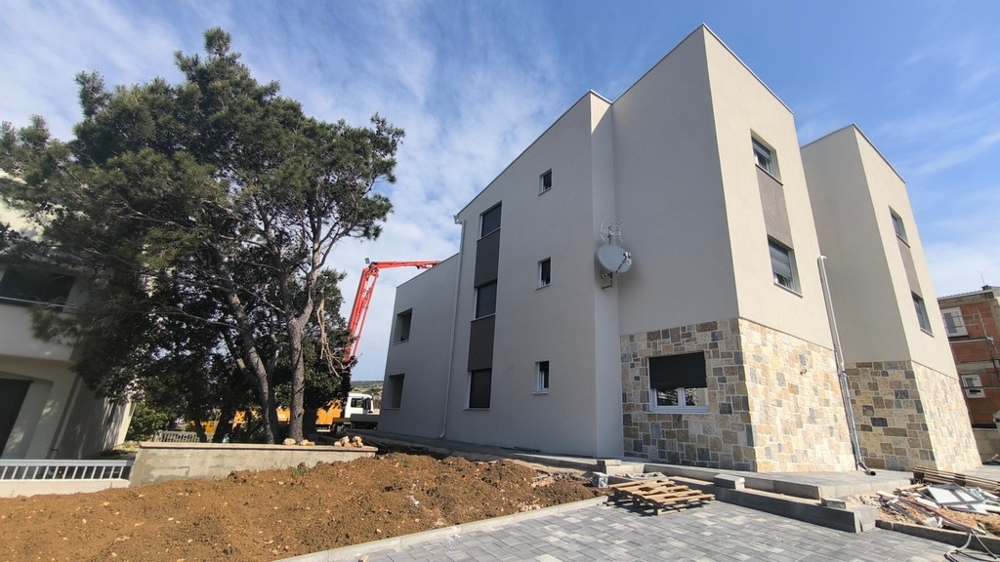 Új építésű modern penthouse ingatlan Horvátországban Simuniban szabadtéri parkolókkal és egy fával az előtérben.