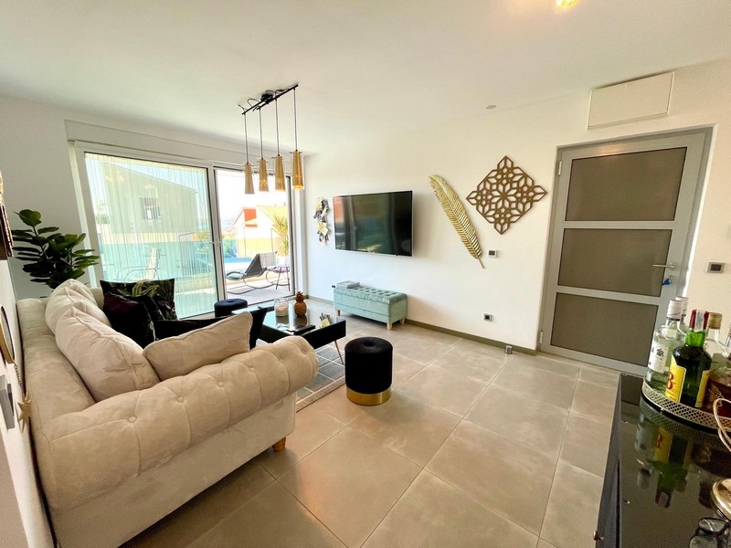 Légkondicionált nappali világos kanapéval és TV-vel.