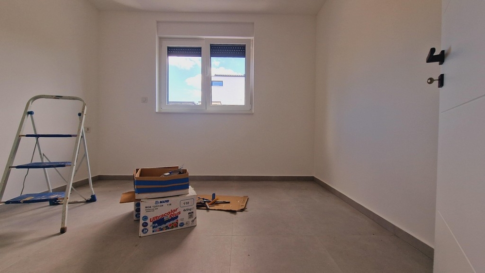 Bútorozatlan szoba szürke padlóval, létrával és költöztető dobozokkal