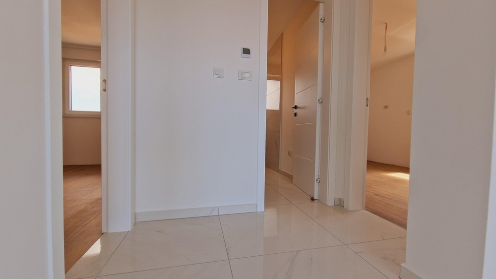 Egy lakás folyosója fehér csempével és több ajtóval különböző szobákba
