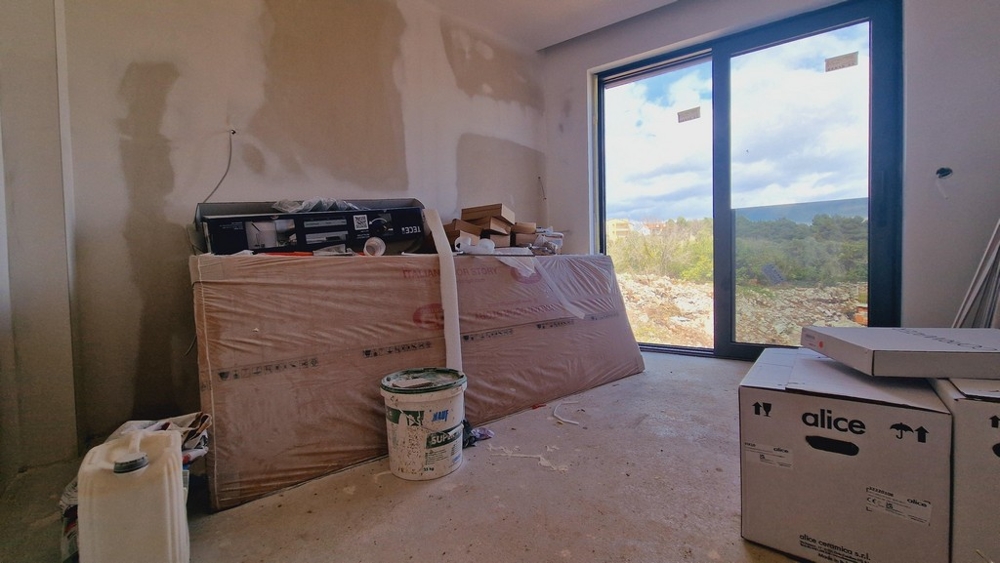 Befejezetlen szoba építkezési anyagokkal és egy nagy ablakkal, amely a tájra néz.