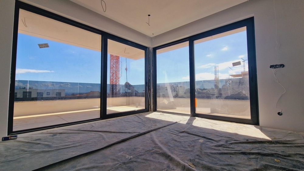 Nappali két nagy üvegfallal, amelyek sok természetes fényt engednek be, és kilátást nyújtanak a környező területre.