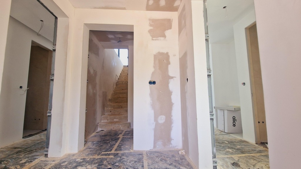 Építés alatt álló lépcsőház és folyosó látható héjfalakkal és nyitott kábelekkel.