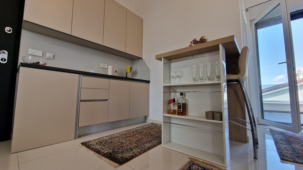 Kicsi, modern konyhasarok beépített polcokkal és bárszékekkel, kijárat a teraszra.