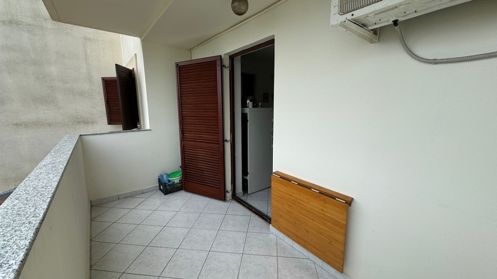 Terasz csempézett padlóval, kilátással a lakás bejárati ajtajára, fehér falak.