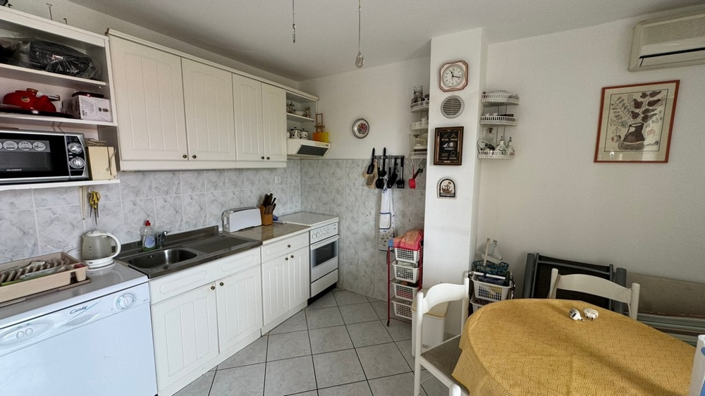 Nyitott konyha fehér konyhasarokkal, étkezővel és a falakkal kis polcokkal.