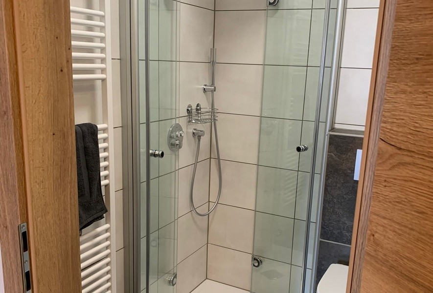 Fürdőszoba modern üvegzuhannyal és törölközőmelegítővel.