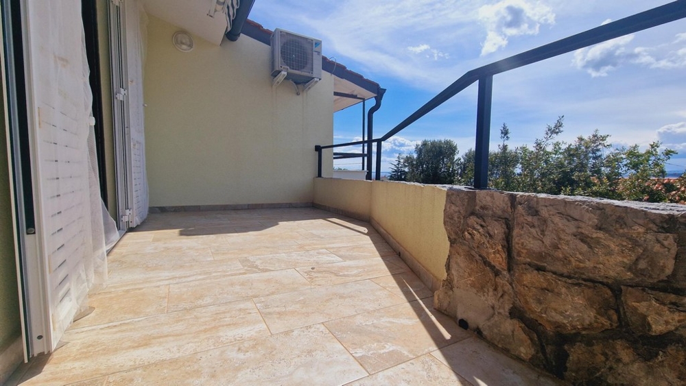 Napos terasz kőfallal, kilátással a környező növényzetre és az égboltra.