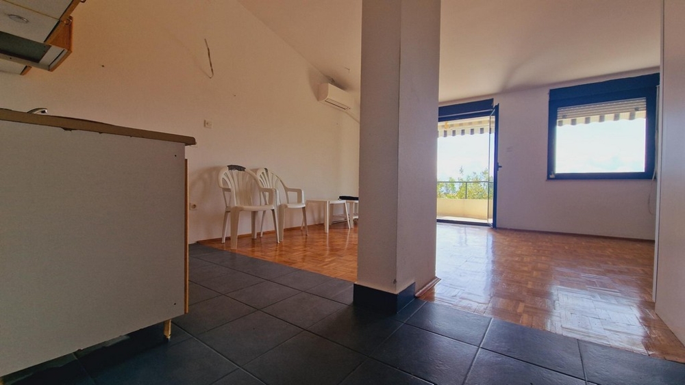 Nappali nyitott konyhával, egyszerű fehér bútorokkal és csempézett padlóval.