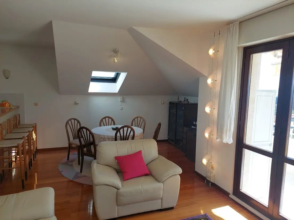 A tetőtéri lakásban étkezőasztal, a konyhapultnál nagy ablakok és bárszékek