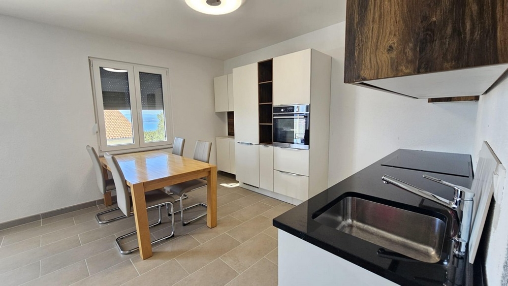 Világos konyha étkezőasztallal, modern berendezésekkel és tengerre néző ablakkal.