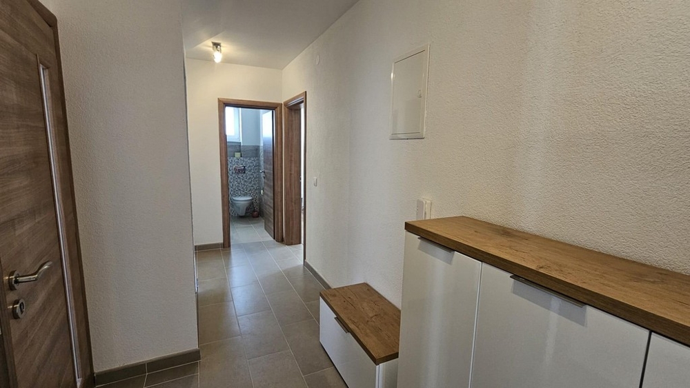 A fürdőszobába vezető folyosó csempézett padlóval és fa díszítéssel.