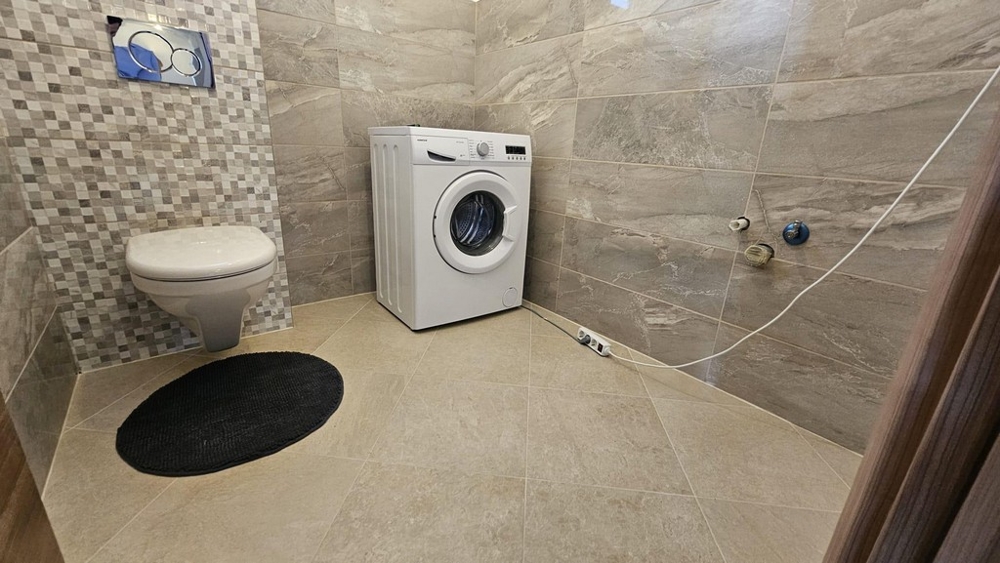 Fürdőszoba mosógéppel, wc és csempézett falak.