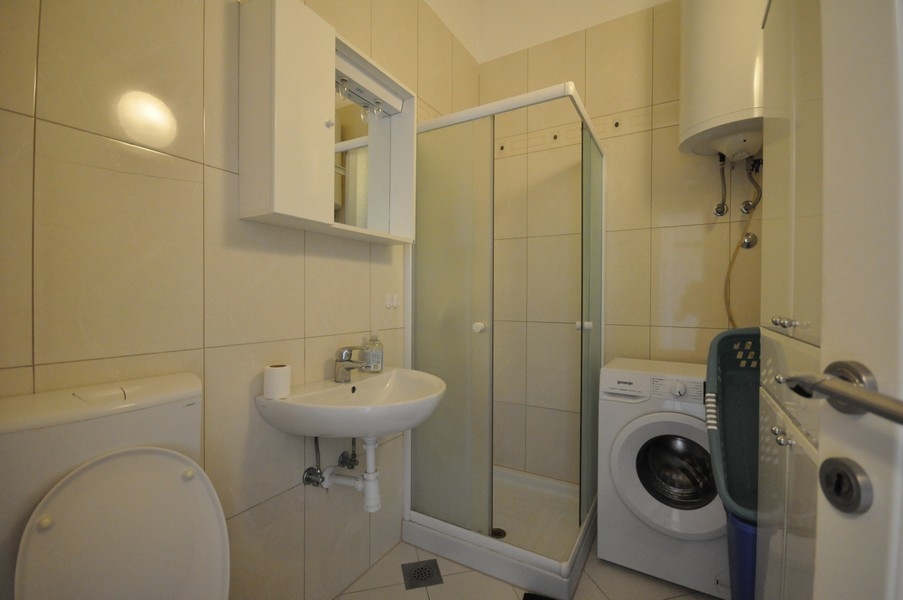 Fürdőszoba zuhanyzóval, mosdóval, WC-vel és mosógéppel, világosan csempézett falak és padló