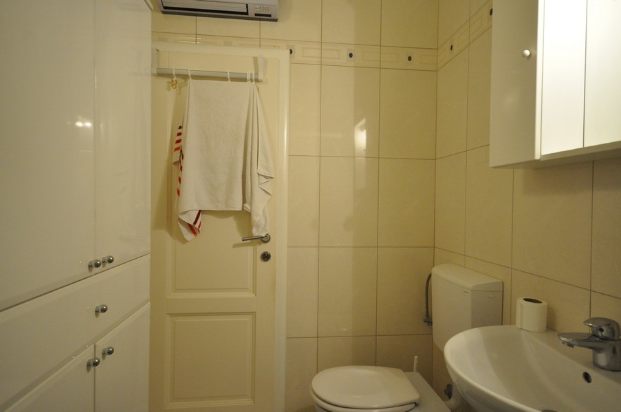 Fürdőszoba WC-vel, mosdó, törülközőtartó az ajtón, világos csempék, modern berendezés