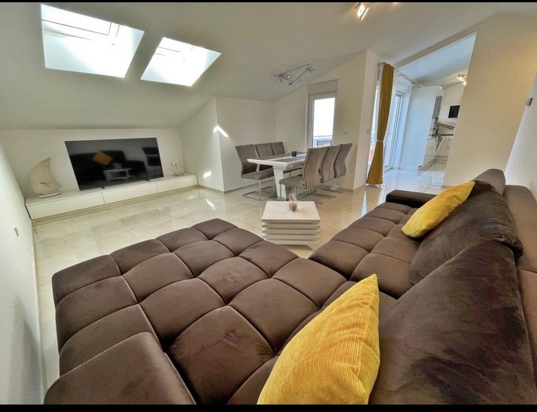 Modern nappali tetőablakkal, nagy kanapéval, étkezőasztallal és televízióval.