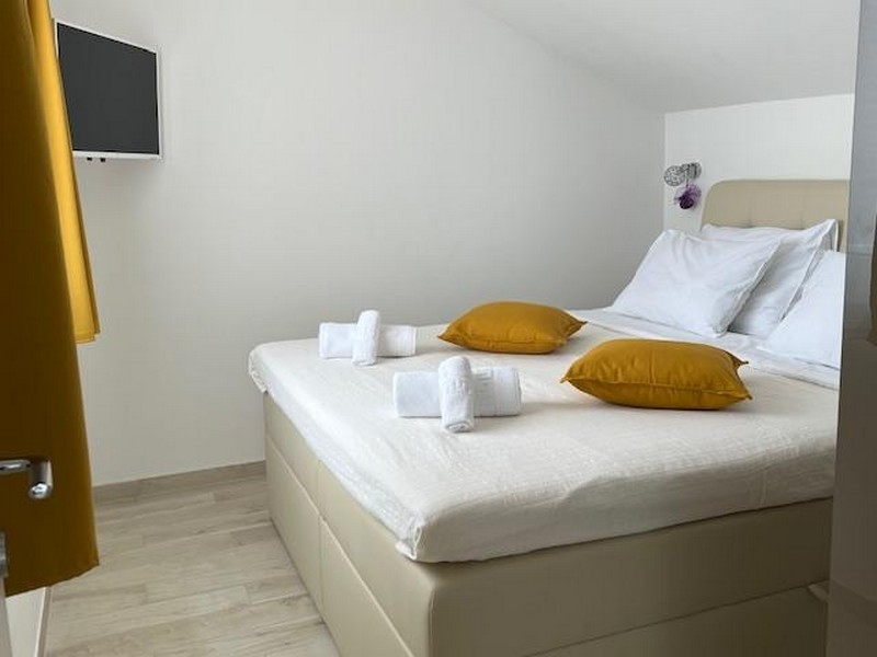 Hálószoba nagy ággyal, sárga párnákkal és televízióval a falon.