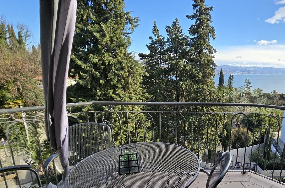 Erkély asztallal és székekkel, fákkal körülvéve, kilátással a tengerre Abbáziában.