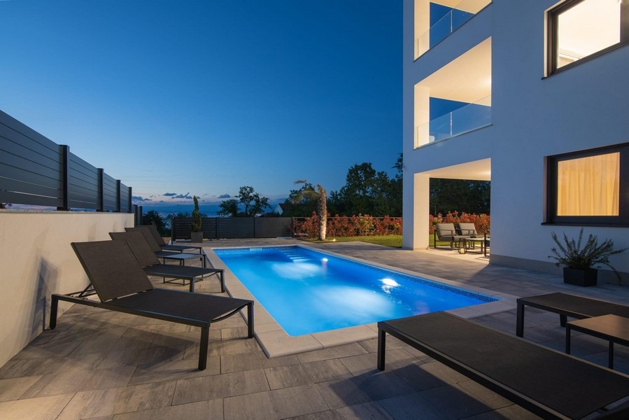 Éjszakai felvétel a megvilágított medencéről nyugágyakkal