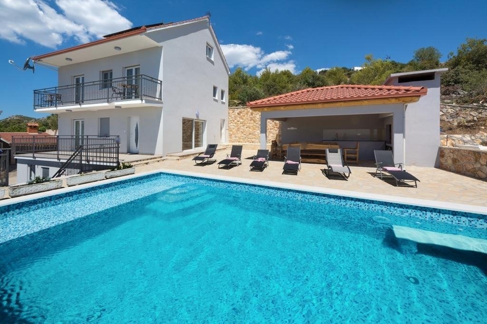 Kilátás a végtelenített medencére, a társalgóra fedett étkezővel és a házra.