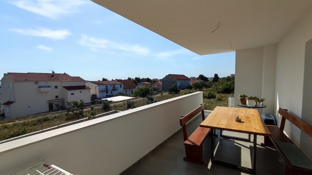 Tágas erkély étkezővel egy családi házhoz Vodicében, Horvátországban, kilátással a csendes környékre.