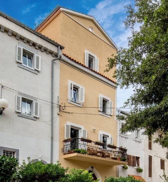 Horvátországi ingatlan részeként egy sárga ház homlokzata, erkélyekkel, redőnnyel