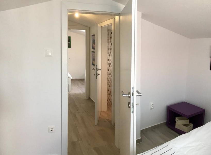 Világos hálószoba a kőház felső emeletén franciaággyal, fehér komóddal és éjjeli lámpával