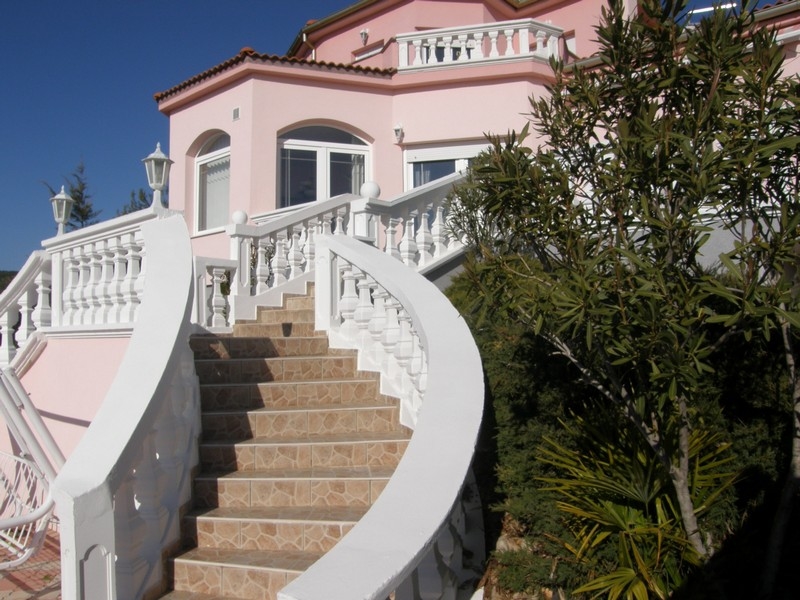 A horvátországi rózsaszín villa elölnézete kanyargós fehér lépcsőkkel és mediterrán növényzettel