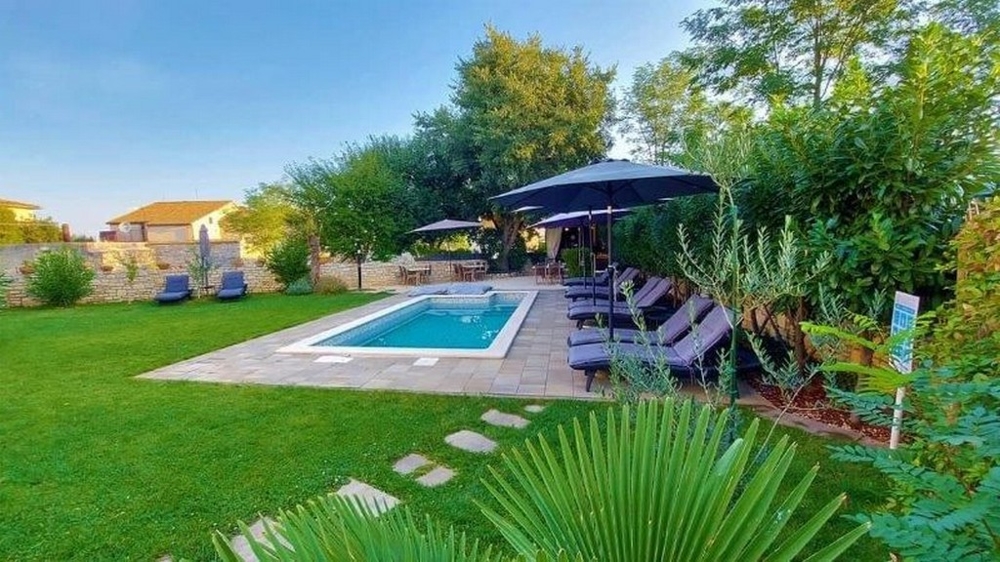 Isztriai háromlakásos ház kertre néző, úszómedencével, napozóágyakkal, napernyőkkel és buja növényzettel eladó.