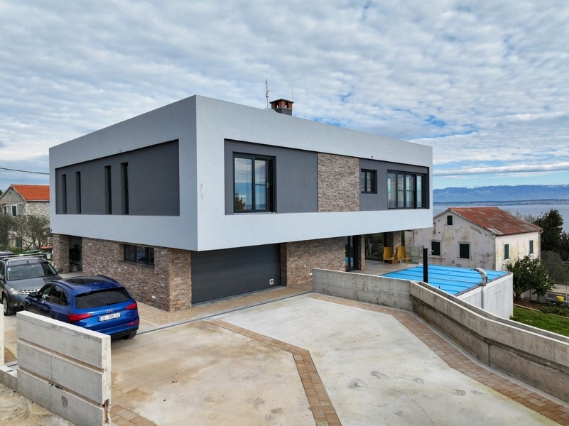A horvátországi Ugljanban eladó egy modern villa garázzsal elölnézete, burkolt felhajtóval körülvéve és részleges kilátással a tengerre