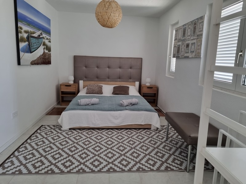 Hálószoba egy bérházban az első sorban a tenger felé, eladó Karlobagban, Horvátországban, nagy franciaággyal, éjjeliszekrényekkel és egy tengeri csónak festményével.