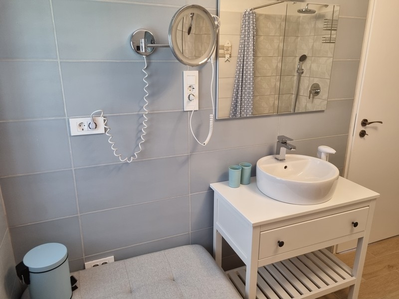 Fürdőszoba egy tengerparti bérházban eladó Karlobagban, Horvátországban, világoskék csempével, fehér mosdókonzollal, tükörrel és törölközőtartóval