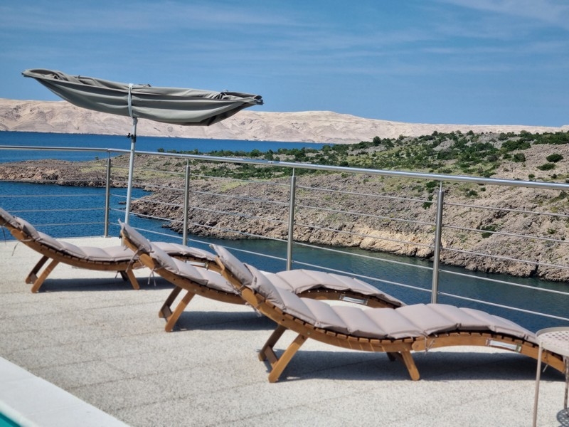 Relaxációs rész nyugágyakkal és napernyőkkel egy apartmanház teraszán a horvátországi Karlobagban, tengerre néző kilátással.