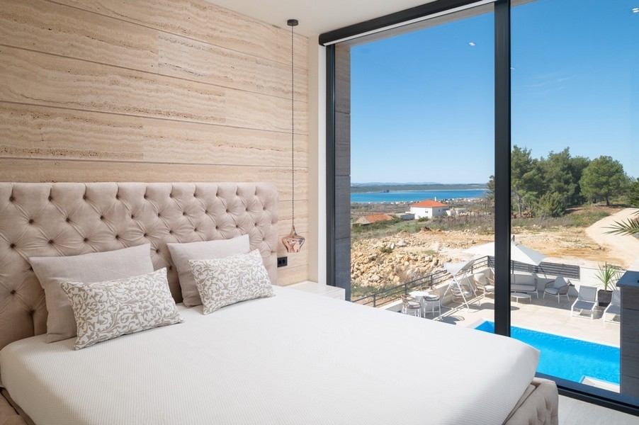 Elegáns hálószoba egy villában Razanacban, Zadar régióban, Horvátországban, nagy ággyal és fejtámlával, tengerre néző kilátással és hozzáféréssel a medencéhez.