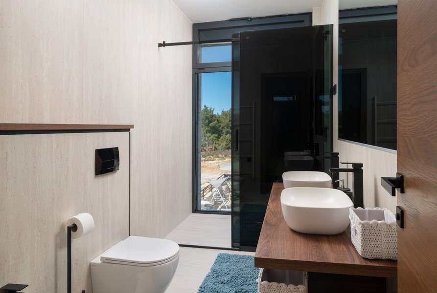 Stílusos, tengerre néző fürdőszoba a horvátországi Zadar régióban, Razanacban található eladó villában, falra akasztott WC-vel és modern mosdóval, fa alsó szekrényen.