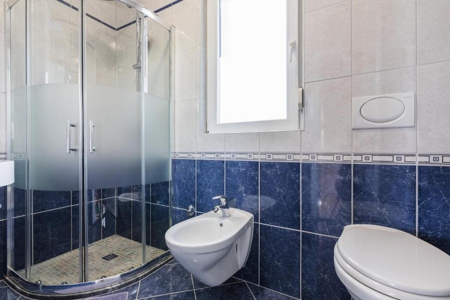 Fürdőszoba egy horvátországi ingatlanban, tengerre néző apartmanházban, sarokzuhannyal, bidével és WC-vel, világos falakkal és sötétkék csempével