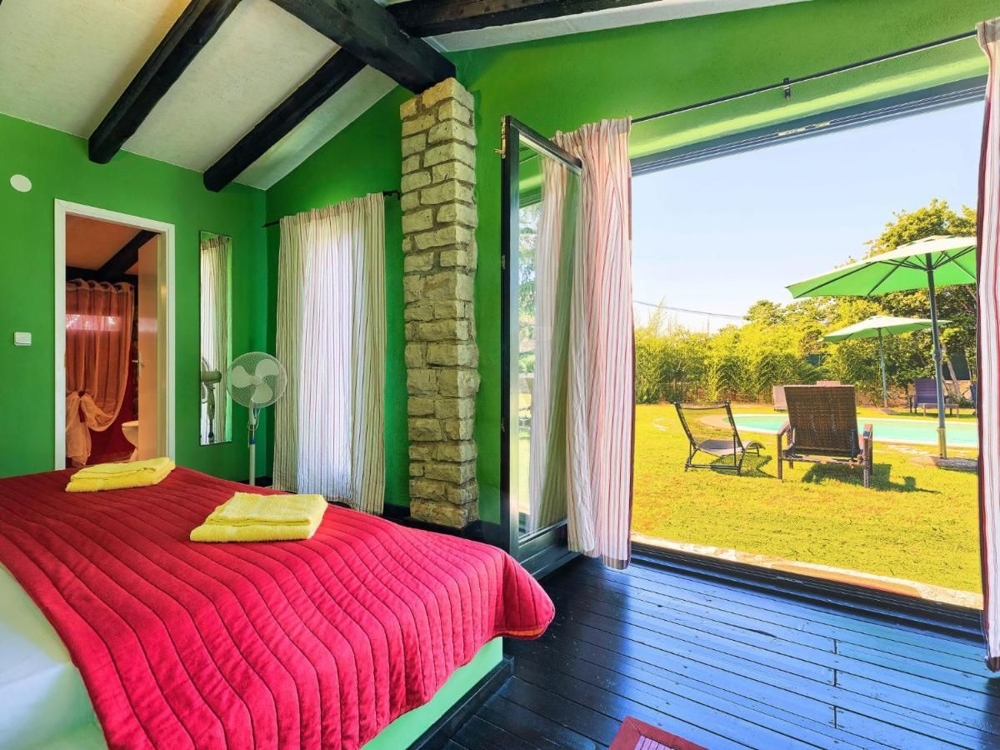 Világos hálószoba kertre néző kilátással, egy horvátországi ingatlan része, zöld falakkal, piros ágytakaróval és hozzáféréssel a teraszra, nyugágyakkal és napernyővel