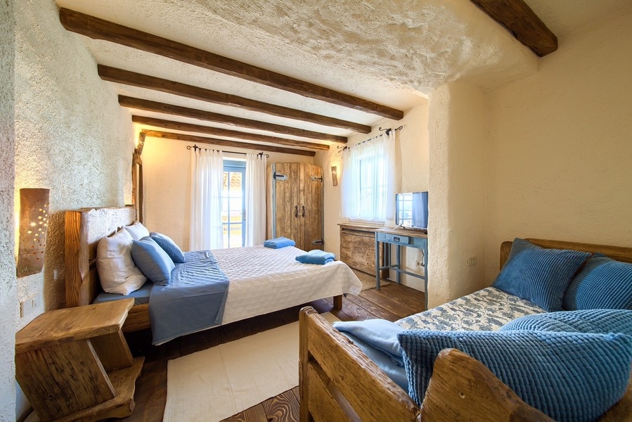 Hangulatos hálószoba rusztikus fabútorokkal és természetes világítással, a Krk-szigeti ingatlan barátságos megjelenésével.