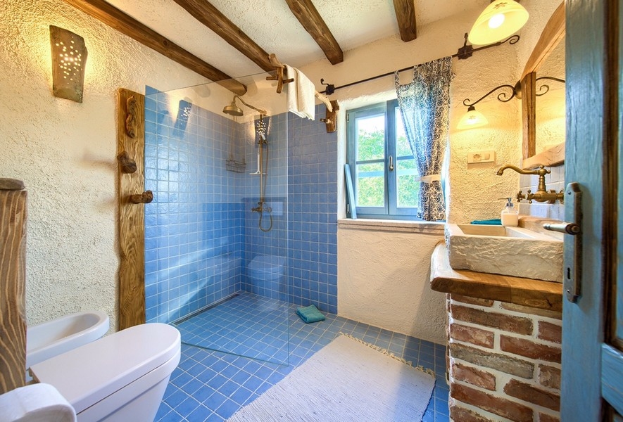 A kék csempével és természetes fa elemekkel díszített fürdőszoba modern kényelmet kínál a Krk-szigeti ingatlanban.
