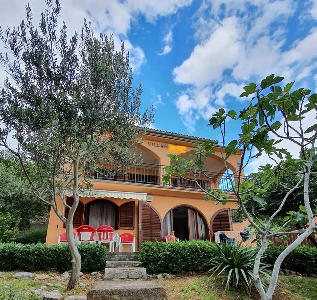 Külső kilátás egy kétszintes villa narancssárga homlokzatával és boltíves ablakaival, fákkal és zöldterületekkel körülvéve