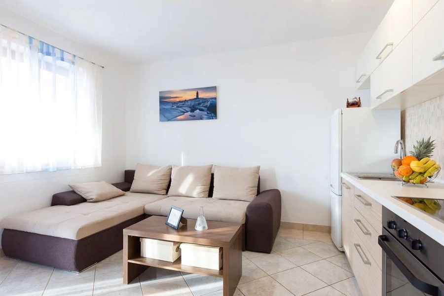 Hangulatos nappali sarokkanapéval, dohányzóasztallal és kilátással a konyhára, lágy színekkel és tenger képével.