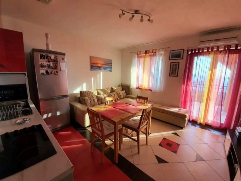 Napsütötte nappali-étkező piros és sárga díszítéssel, étkezőasztallal, kanapéval és kijárattal az erkélyre.