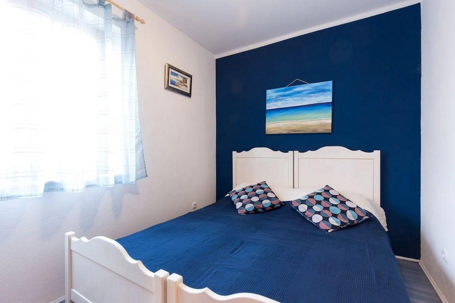 Hálószoba franciaággyal, kék akcentussal és tengeri dekorációval, amelyet az ablakból természetes fény világít meg.