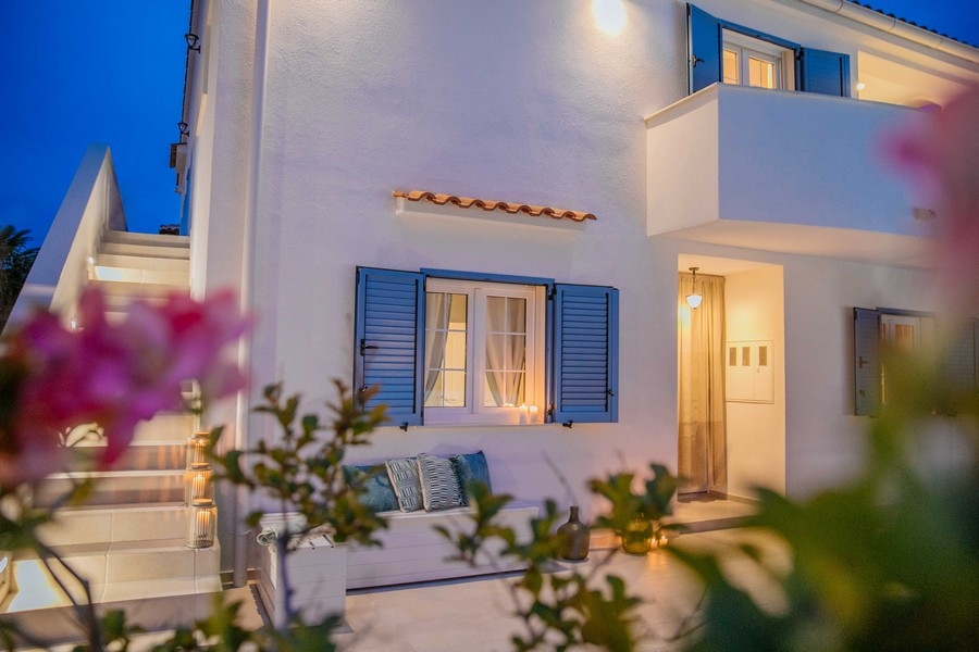 Egy mediterrán ház elölnézete kék redőnnyel és szabadtéri ülősarokkal alkonyatkor, lágy fénnyel megvilágítva