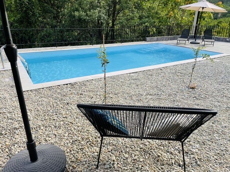 Úszómedence a kertben, kavicsokkal körülvéve, kilátással az erdőre